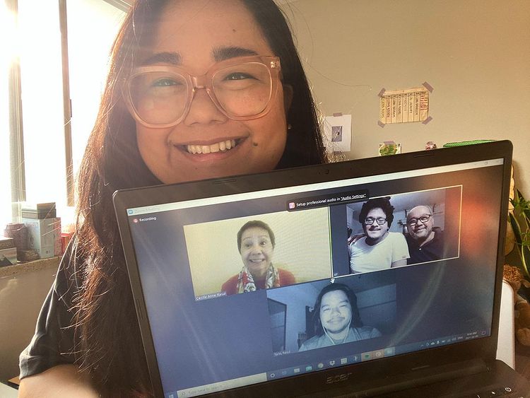 Filipina woman smiling as she holds up her laptop that has a video call with four people in it: an elderly Asian grandmother and three Filipino men, all smiling.