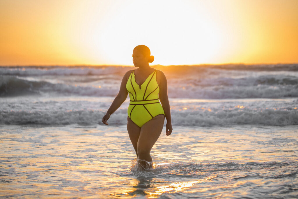 Catherine Li stands the ocean at sunset in a yellow bikini. 