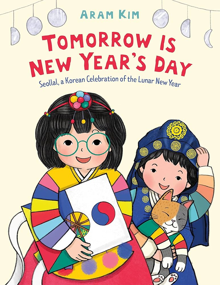 The book cover for Tomorrow Is New Year's Day: Seollal, a Korean Celebration of the Lunar New Year by Aram Kim features two cheerful children dressed in traditional Korean hanbok. The child on the left wears a colorful striped hanbok and green round glasses while holding a white envelope with the Korean flag symbol. The child on the right is dressed in a navy and gold hanbok and lovingly holds a smiling calico cat wearing a small hanbok. Above them, the title is written in bold red and blue text, with a string of moon phases adorning the top of the light cream background. The illustration is vibrant and celebratory, emphasizing the joy of the Korean Lunar New Year.