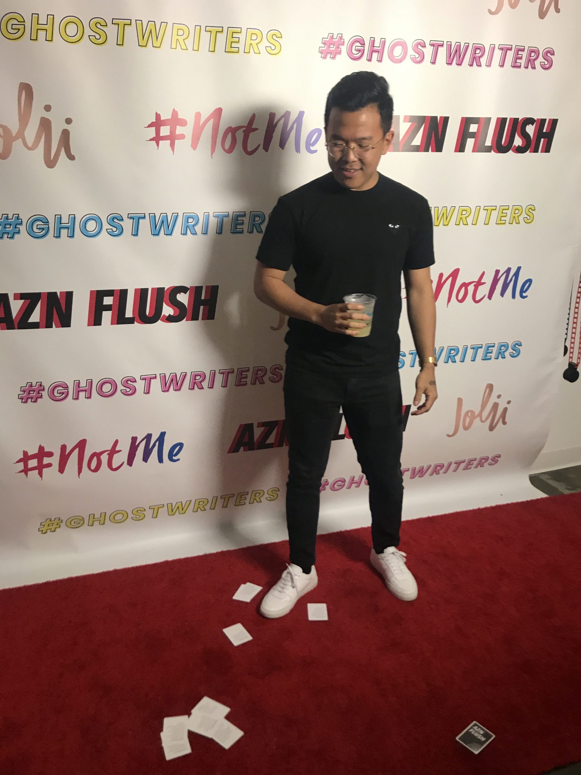 John Lim, creator of AZN Flush standing on a red carpet with cards on the ground. 