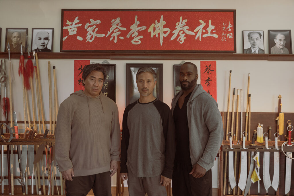 The three lead actors of the Paper Tigers film (Ron Yuan, Alain Uy, Mykel Shannon Jenkins) pose in front of the film's kung fu school.
