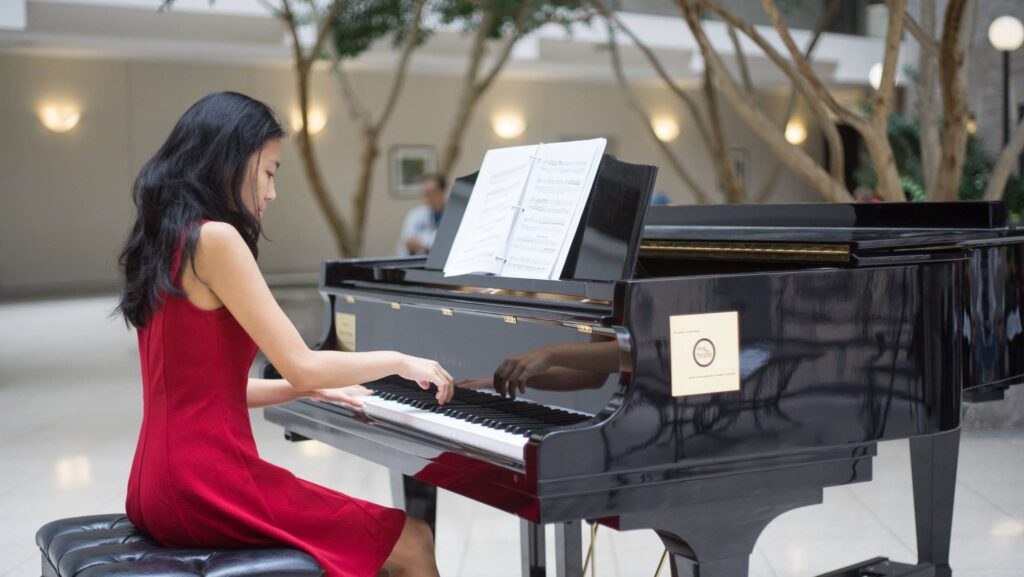 Alice Tsui playing a piano in a red dress