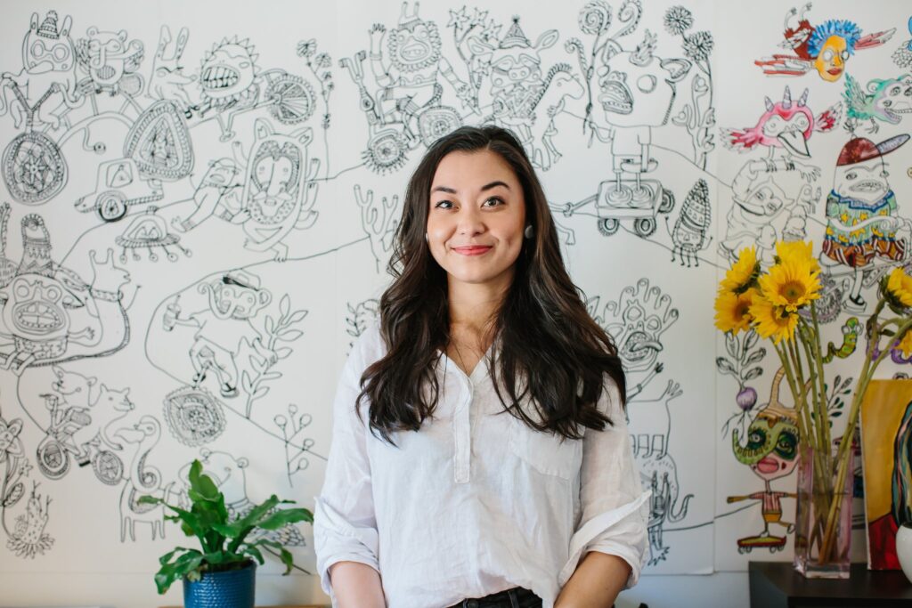 An image of author Chanel Miller sitting in front of a whiteboard with many drawings.