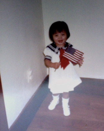 A young Asian girl smiling and holding a mini American flag. 