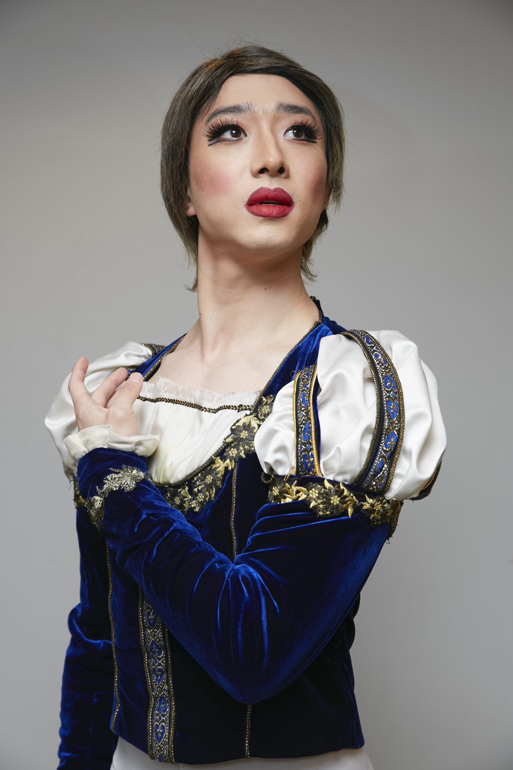 Haojun Xie as Nicholas Khachafallenjar, dressed in a princely blue and white costume, posing and looking up into the distance.