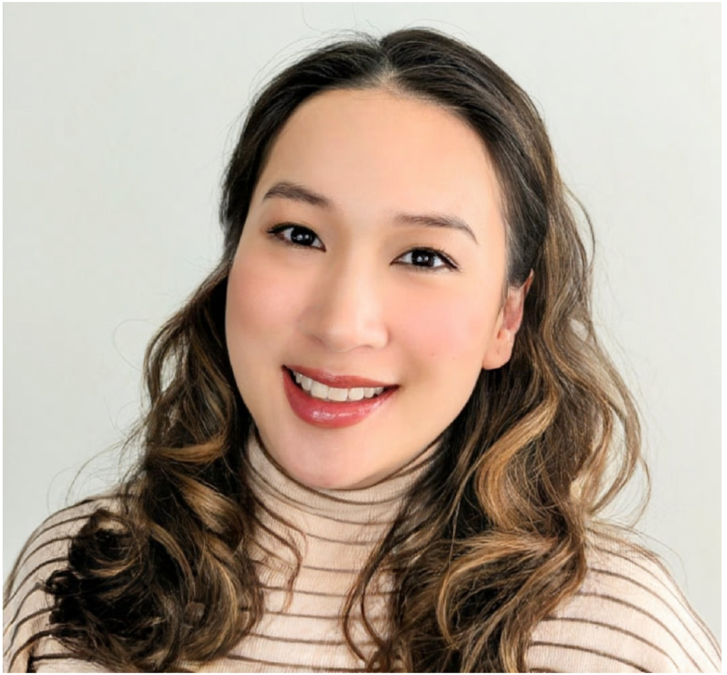 Jenny Mai Phan, a Vietnamese American woman, smiles warmly at the camera. She wears a beige ribbed top and her dark hair is styled in soft curls. The neutral background and lighting give the image a polished, professional tone.