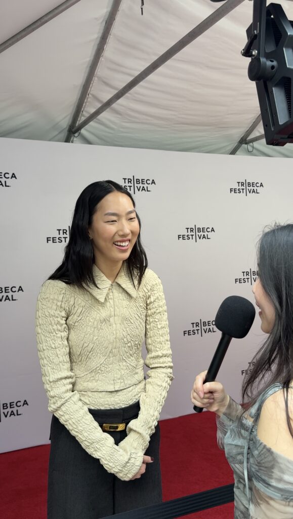 Actress Madison Hu standing on red carpet at Tribeca Film Festival 2025 premiere of Rosemead. She is standing and smiling at journalist Kacie Mei, wearing a yellow sweater and black pants with hands clasped in front of her. 