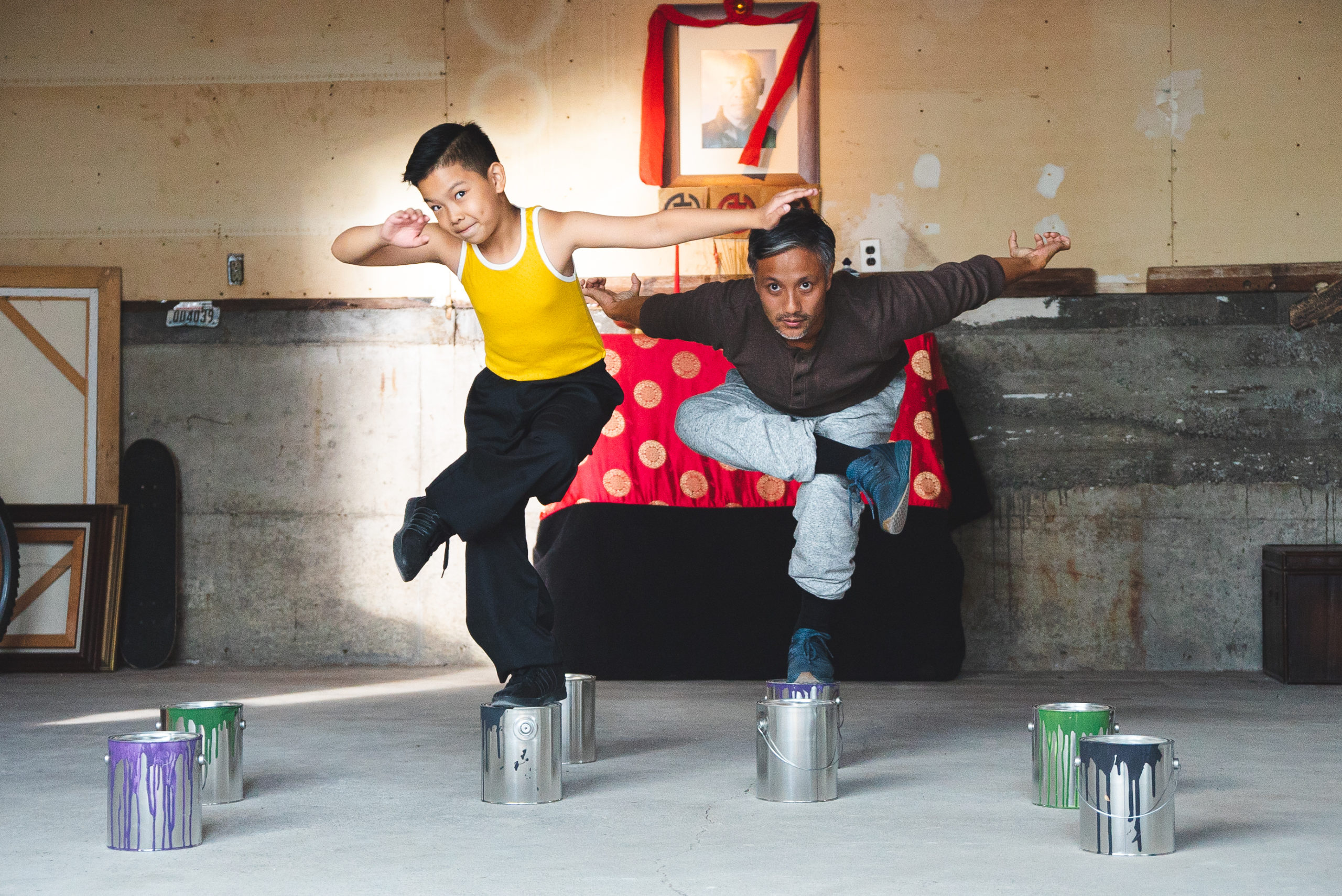 Behind the scenes of The Paper Tigers film, featuring actors Joziah Lagonoy and Alain Uy posing one-legged on cans of paint