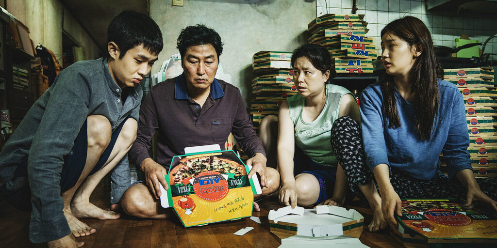 a family of four (son, father, mother, daughter) sit on the floor surrounded by pizza boxes looking down and at each other, as if mid-conversation
