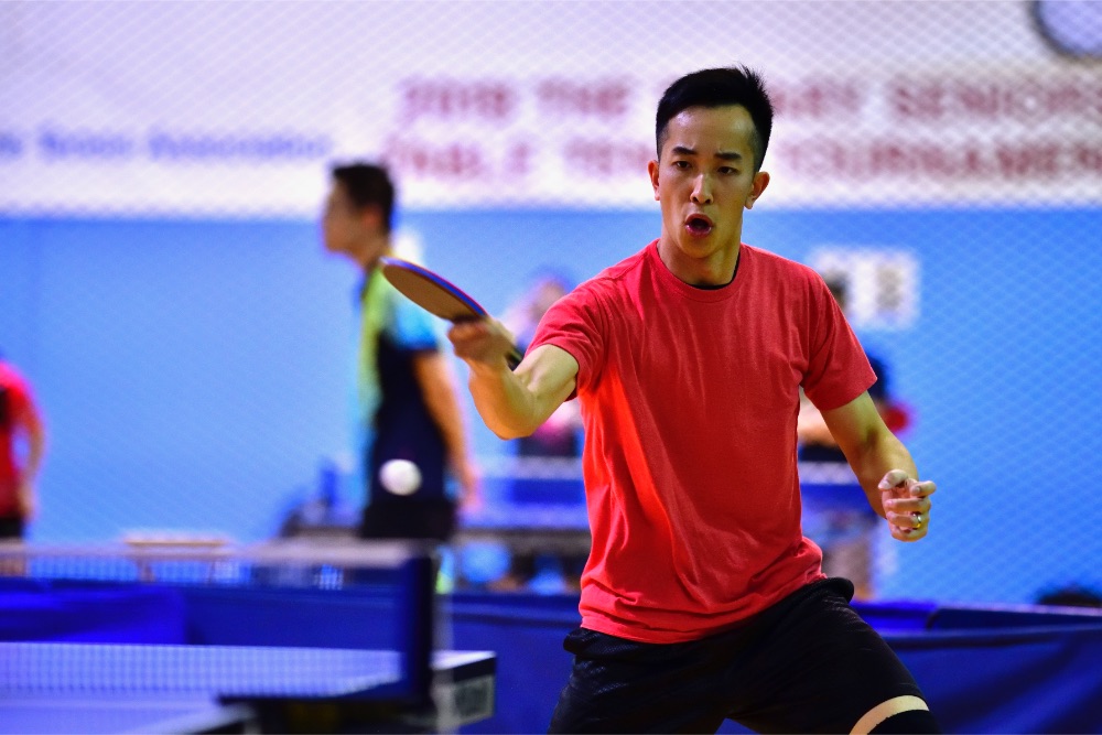 an action shot of Peter Yau returning a ping pong ball across the table