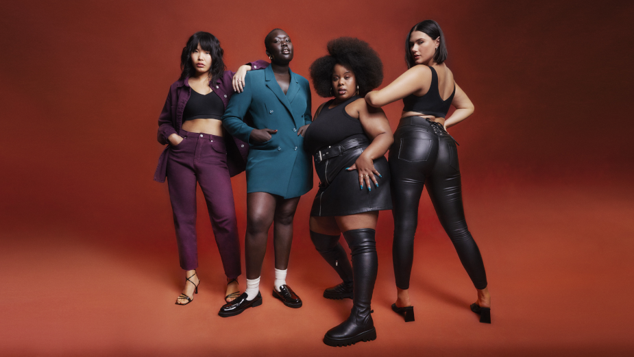 Four women affirm body positivity in a photoshoot. The outfit colors are darker, with black, purple and blue. 