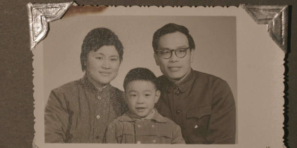 a faded photograph in a photo album of a family of three, of a young son in between his two parents, smiling in the camera's general direction