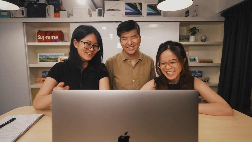 Three asian people sitting before a screen, laughing. 