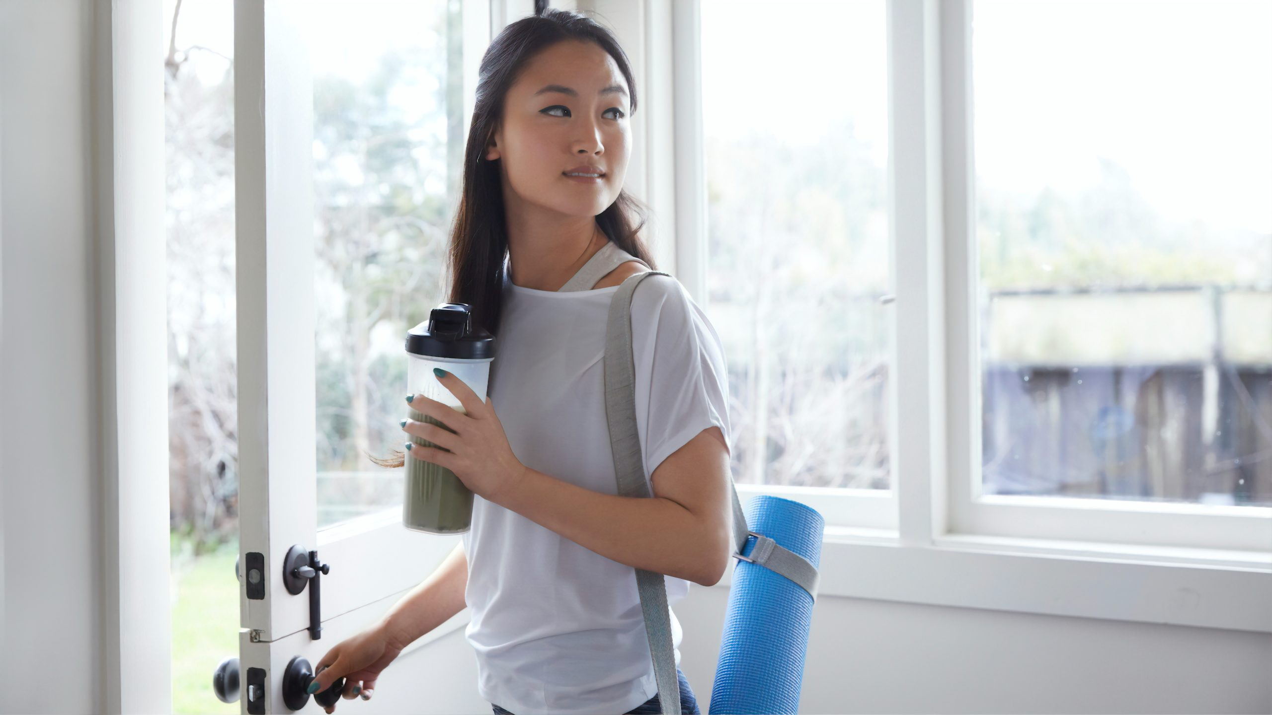 Asian women holding protein shake and yoga mat.