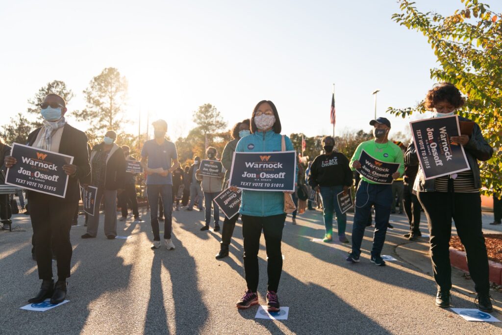 Asians holding signs supporting Warnock and Jon Ossoff. 