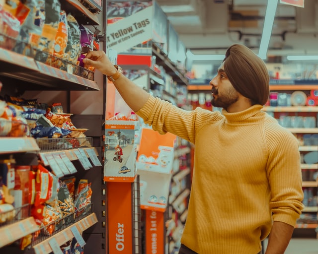 A turbaned brown Asian man is shopping for chips at a supermarket. 