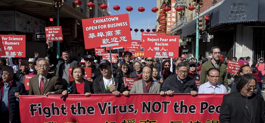 People holding a sign that says "Fight the Virus, NOT the People" in Chinatown as well as other smaller signs that say "Chinatown open for business" and "Reject Fear and Racism"