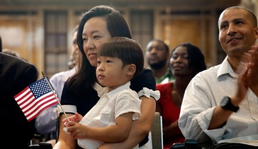 Asian mother holds her younger son who is holding an American flag. The room is surrounded by other people who look happy. 
