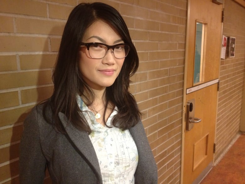Author Jenny Heijun Wills standing in front of a brick wall, looking at the camera