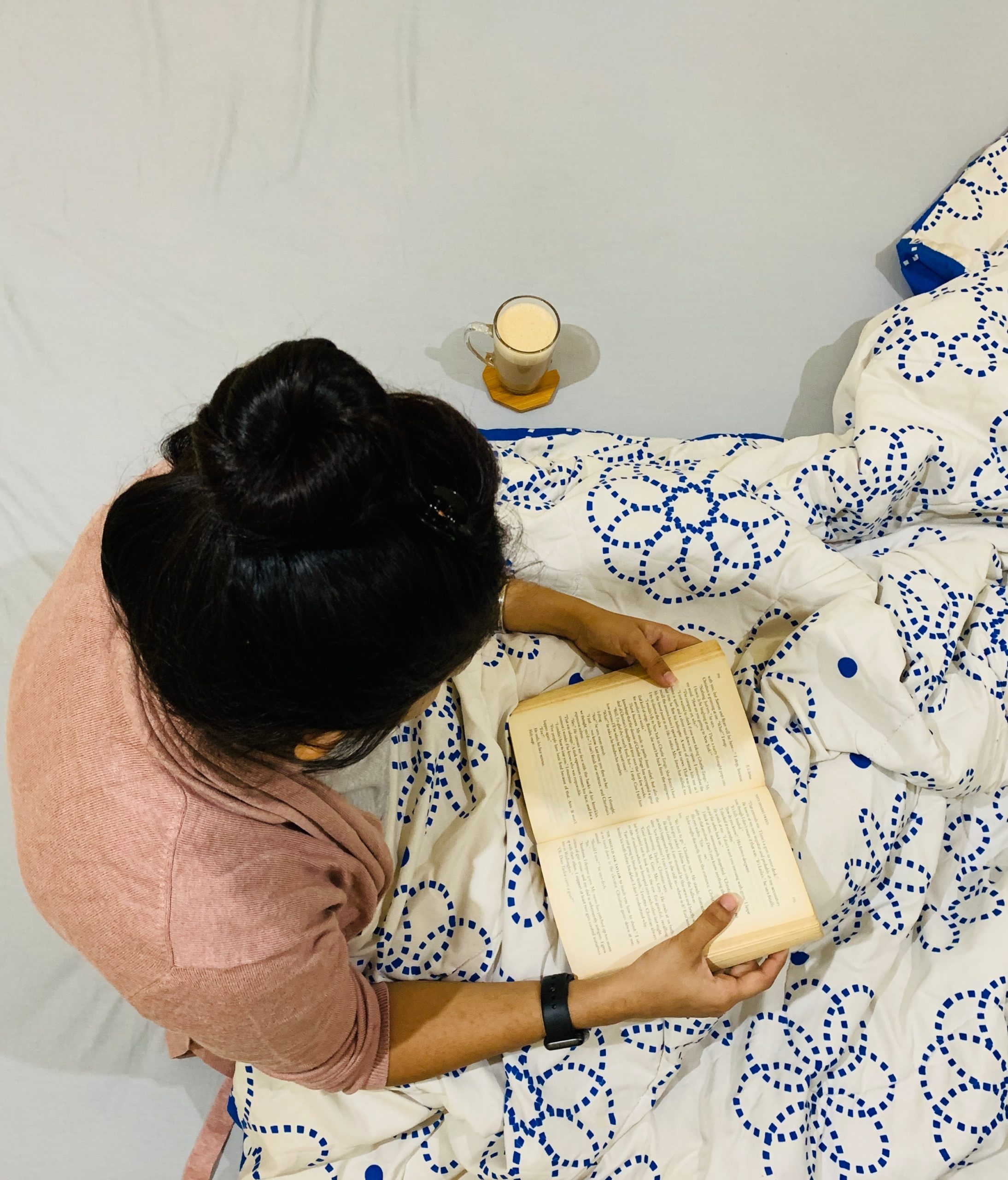 Image shot from above of a woman sitting under a blanket, reading a book. 