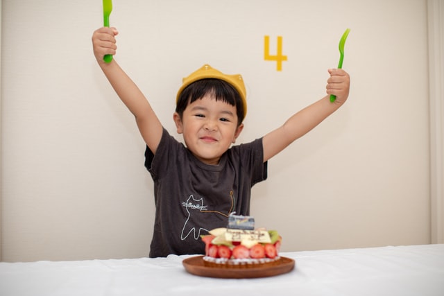 4 year old birthday boy raising his hands in front of a cake. 