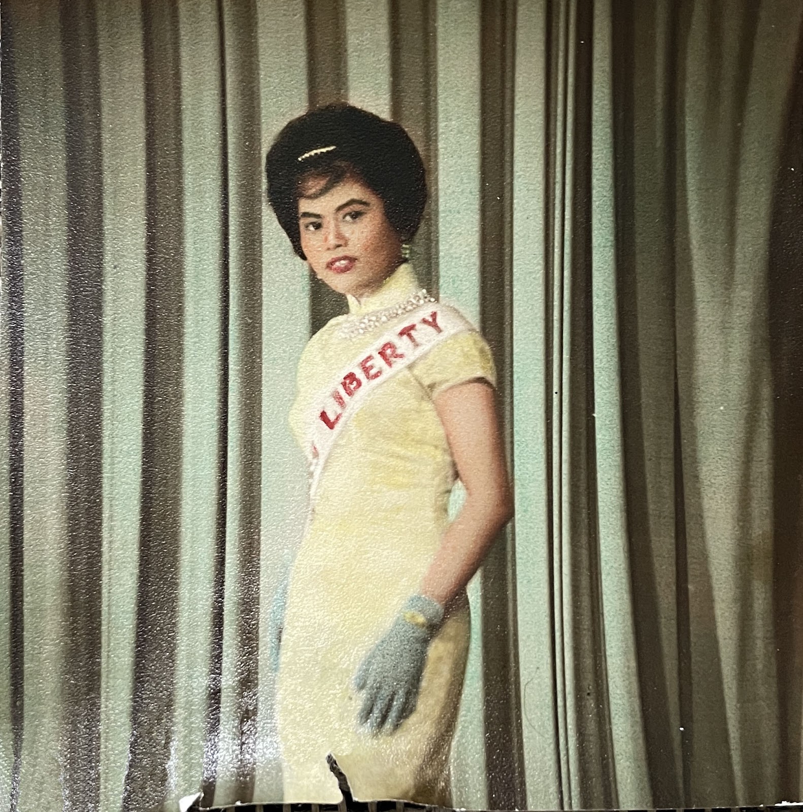 An image of the author's grandmother competing in a beauty pageant, standing in front of a green curtain.
