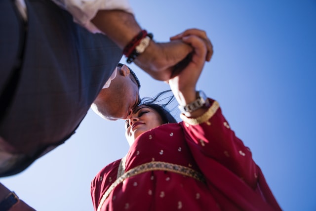 Photo of Indian couple clasping both hands and touching foreheads taken from an low angle looking up. 