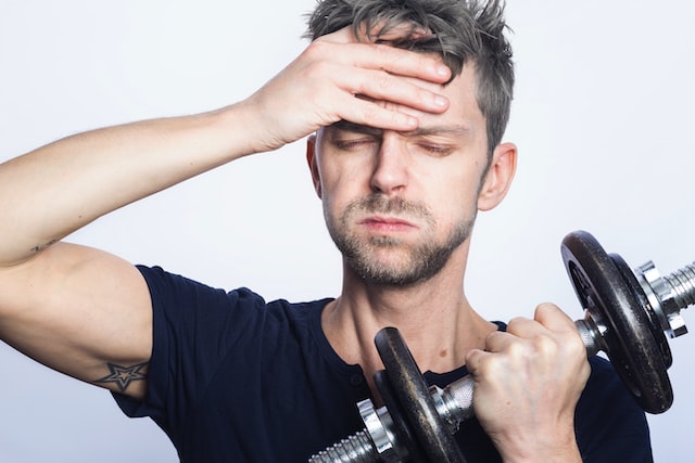 Man holds dumbbell and looks stressed, bringing up concerns of mental health. 