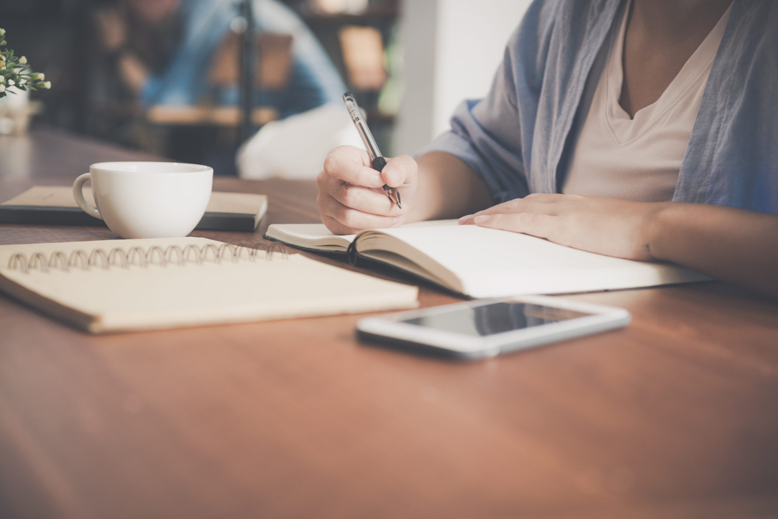 Young business woman in white dress sitting at table in cafe and writing in notebook